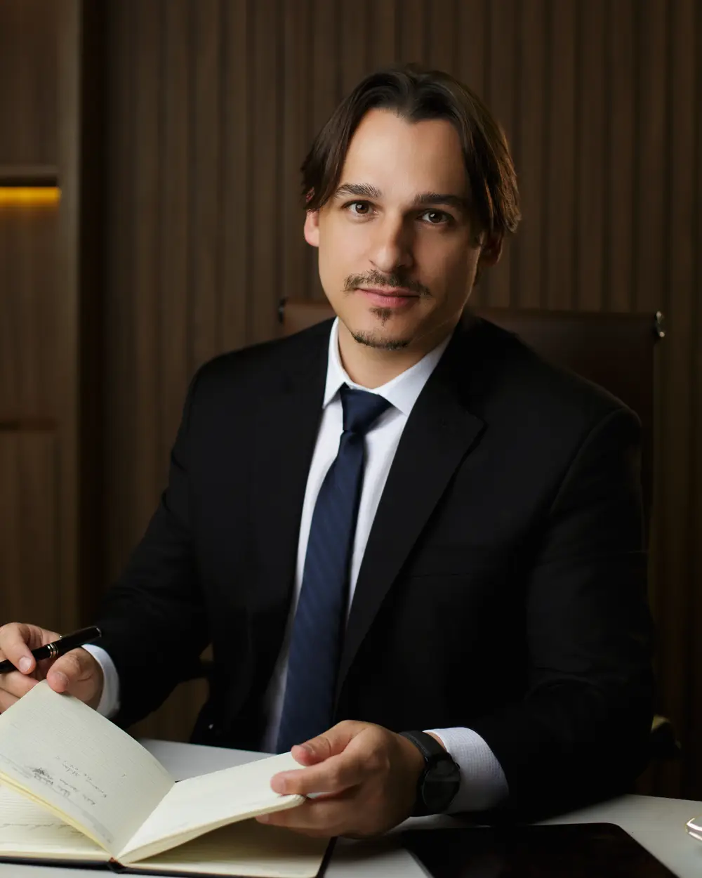 Rafael Dantas de terno, à mesa do escritório, anotando num caderno